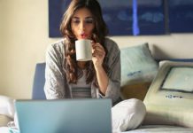 What Are the Essential Elements for a Functional Home Office? Work At Home - Woman in Grey Jacket Sits on Bed Uses Grey Laptop