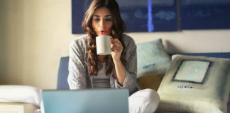 What Are the Essential Elements for a Functional Home Office? Work At Home - Woman in Grey Jacket Sits on Bed Uses Grey Laptop