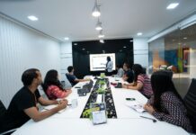 Why Is MaxMunus the Right Choice for Lenel OnGuard Training? people-sitting-at-the-table-looking-to-another-person-standing-in-front-of-them